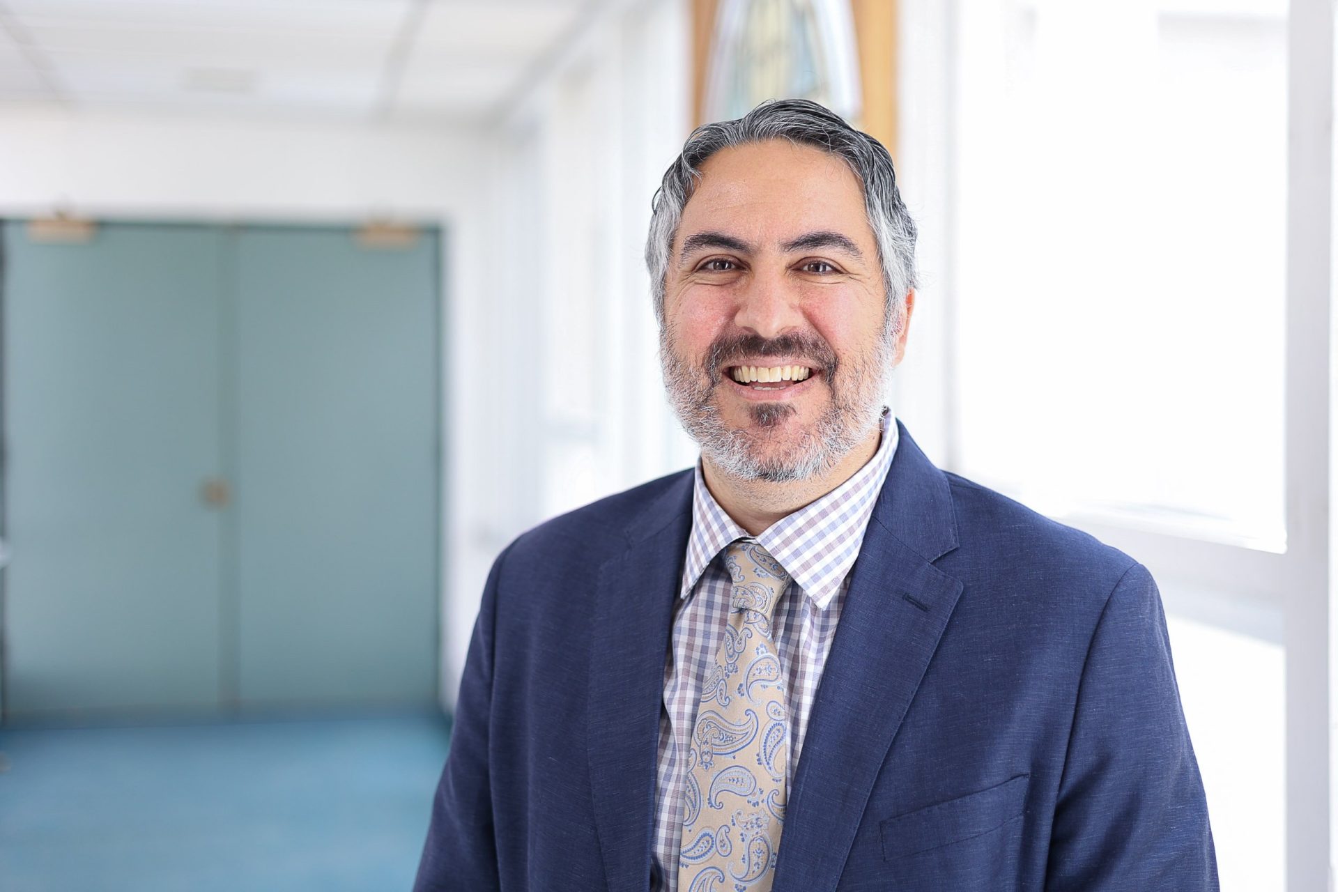 Mark Signorelli, a confident professional in a suit, smiles warmly in a bright office setting.