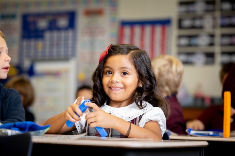 Young girl joyfully engaged in creative learning at a colorful classroom desk.