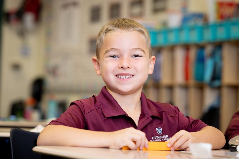Joyful boy in maroon shirt engaged in creative classroom activities at Livingston Classical Academy.