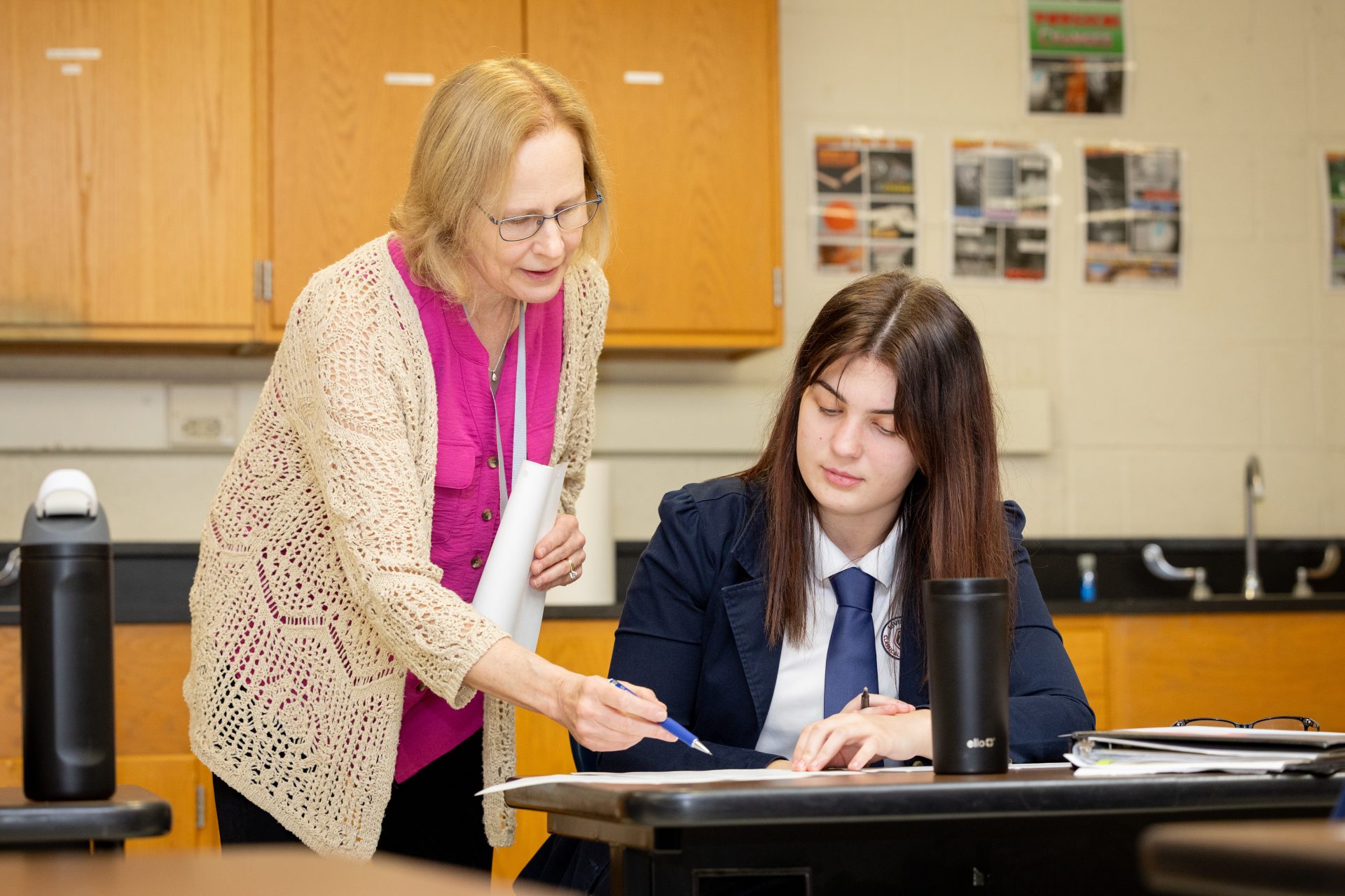 Instructor guiding student in engaging classroom, promoting collaboration and effective learning in education.